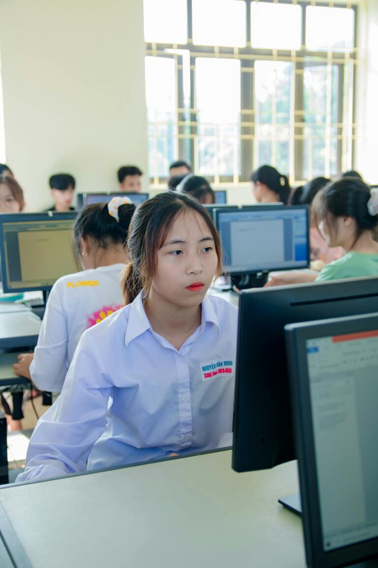 Asian woman focused on computer screen in a modern office with colleagues.
